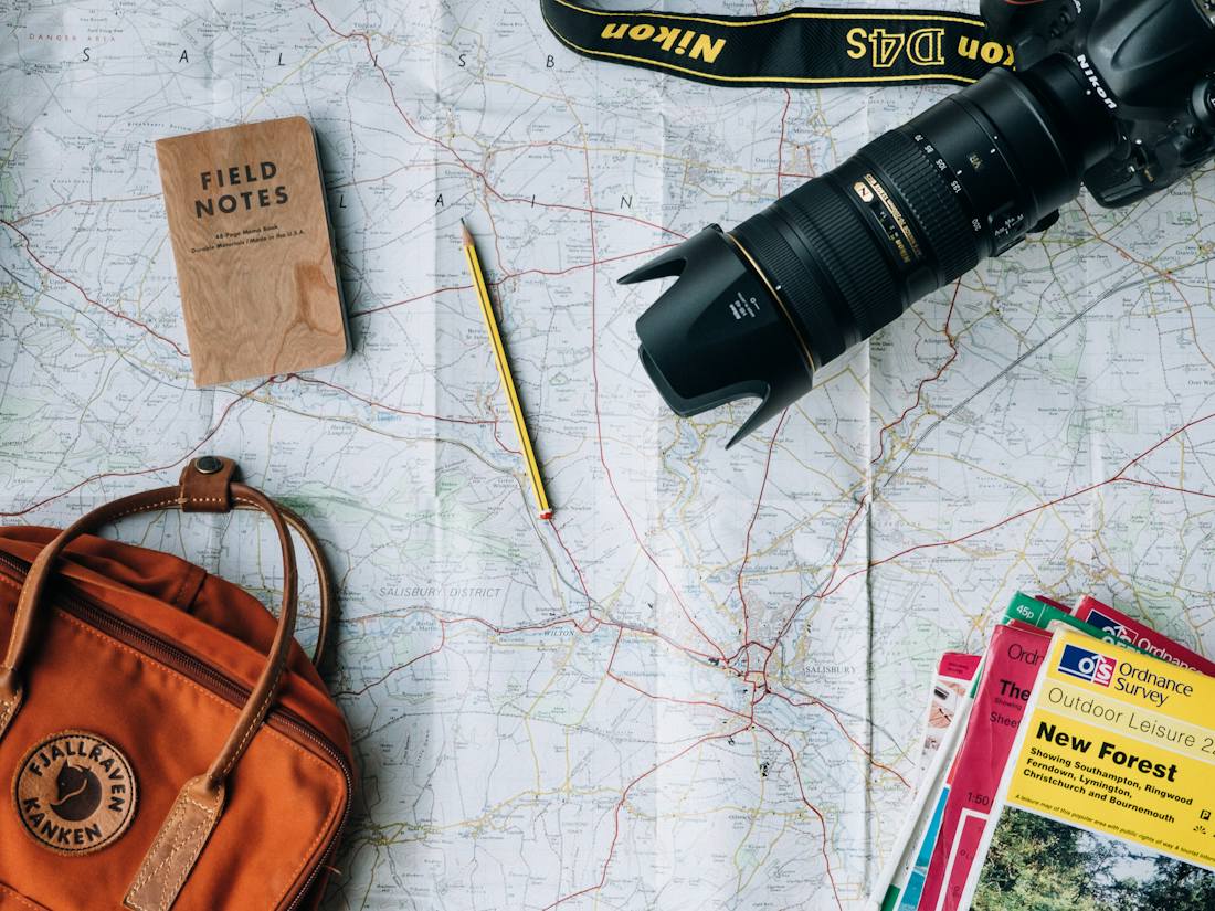 Mapa, mochila, cámara y libreta de viaje sobre una mesa